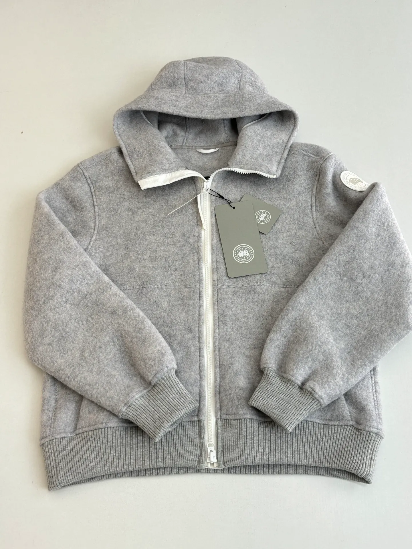 P810 Canada Goos*/Big Goose Fleece Badge Hooded Jacket The fabric is made of wool as the main body, with a very small amount of spandex and polyester fiber blended into the wool fleece fabric. The sleeves and hem are closed with 2×2 ribbing. Its strong elasticity can closely fit wrists and waists of different thicknesses, forming an effective 'seal' to prevent cold wind from blowing back. It can still maintain its original shape after repeated stretching and use, and is not easy to loose and deform. And the ribbed cuffs can convey a sense of design and enhance the visual beauty.  Size：S/M/L/XL